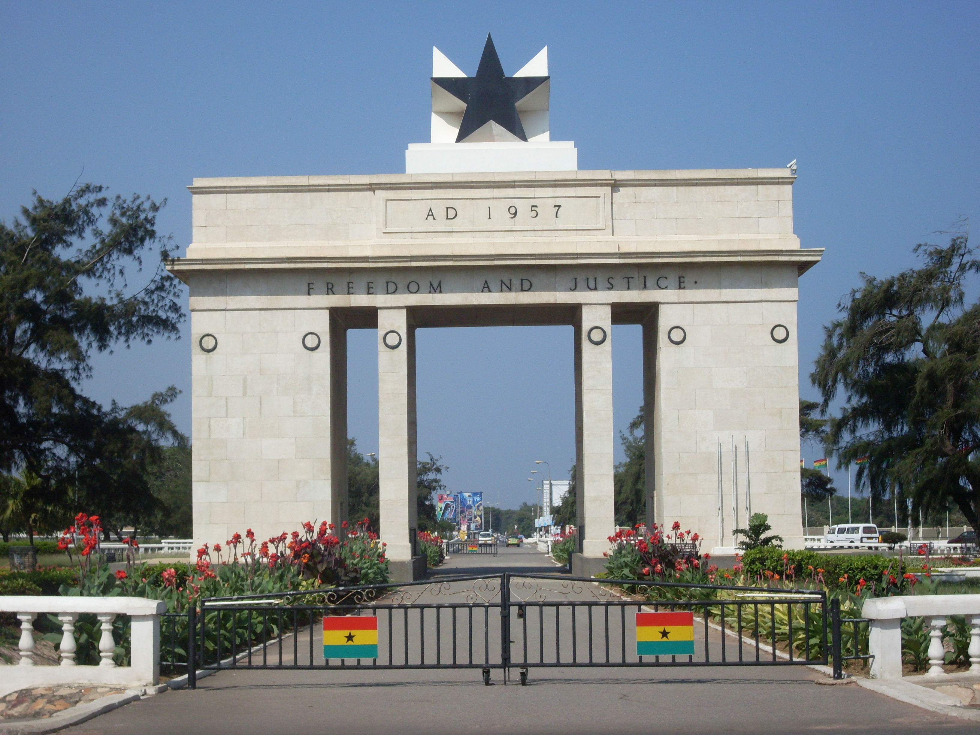 A white stone gate topped by a black star, with Freedom and Justice inscribed across its front and Ghana flags on the entrance gates.