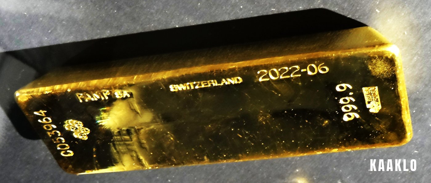 A gold bar stamped PAMP SA, Switzerland, 2022-06 and 999.9 on a dark surface.